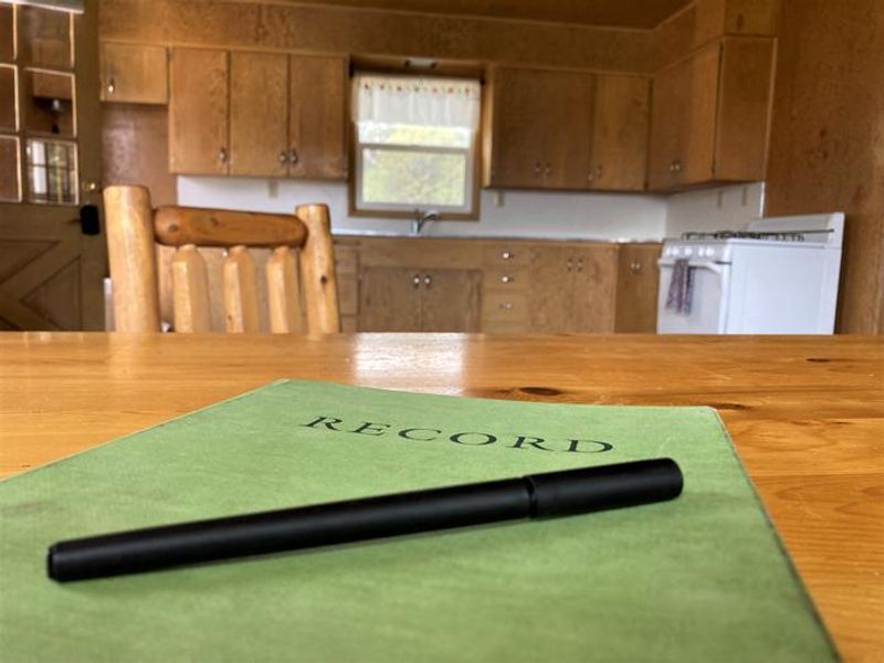 A community records book where occupants write down their experiences and maintenance requests sits atop the dining table of Orange Olsen Dwelling.