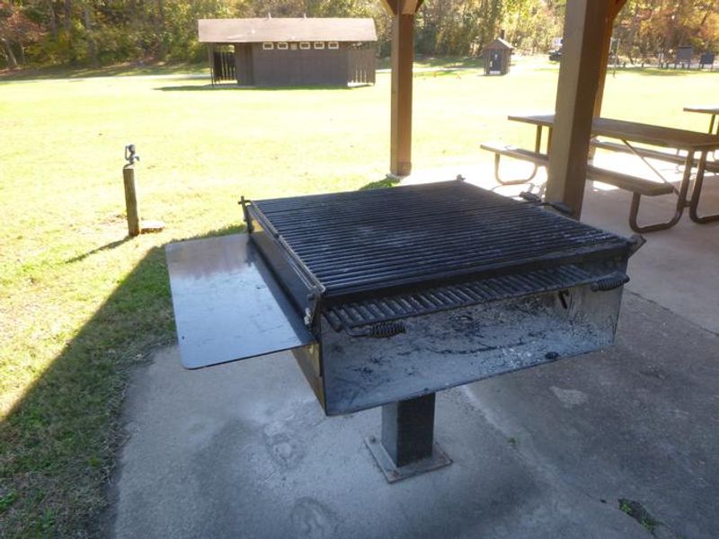 Grill with water spigot, flush toilet and pit toilet in background