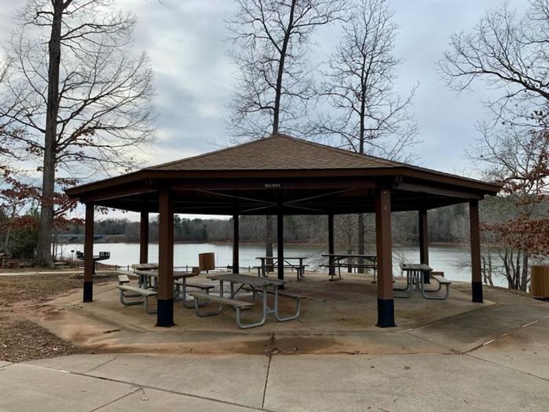 This is the picnic shelter located in the Rudds Creek Day Use Area. There are picnic tables located under the covered shelter. There is a large grill located on the side of the building. There are trash cans located throughout the park. 