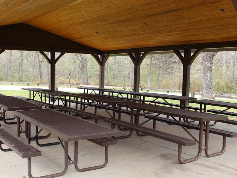 Several picnic tables under the Ozark Pavilion with campsites in background