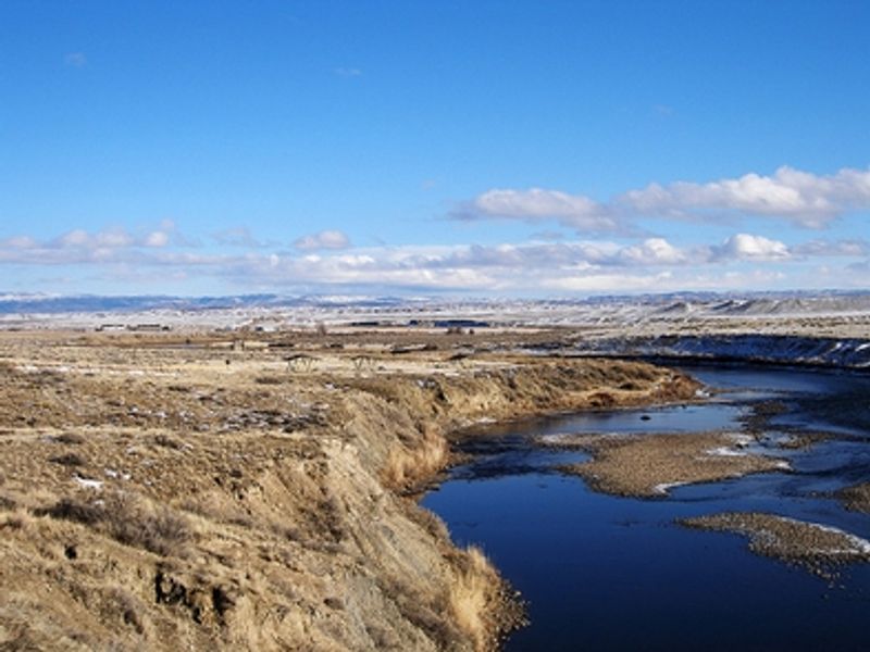 An open valley sits next to a canal, covered picnic tables stand in the distance.