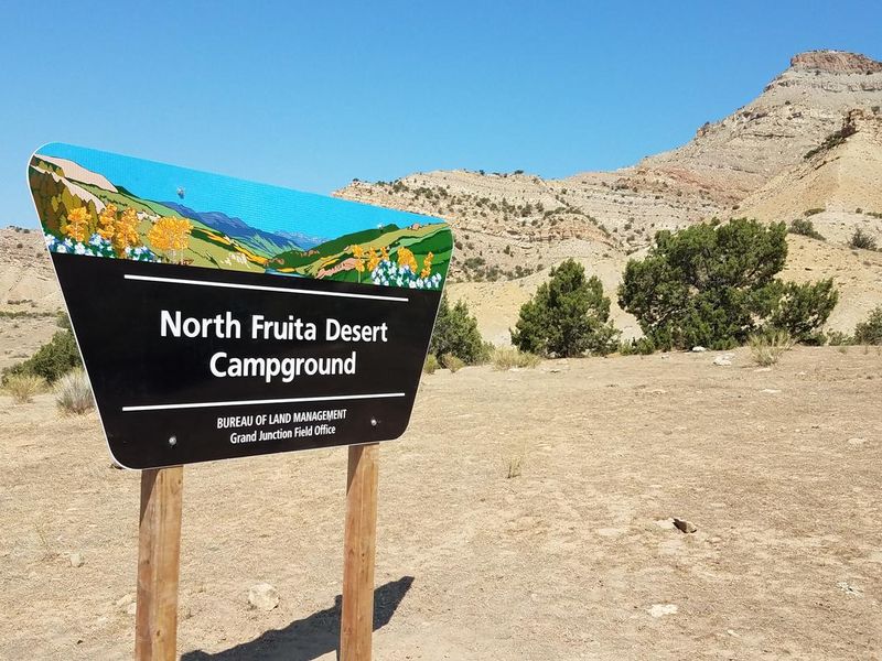 North Fruita Desert Campground sign at entrance to campground.  Bookcliff mountain range in background. 