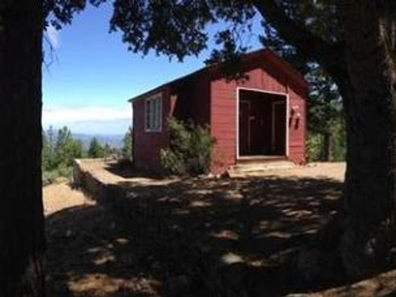 Upon arriving at the cabin, guests will be greeted by this quaint old cabin set among trees, with a view of distant mountains and ridgelines.