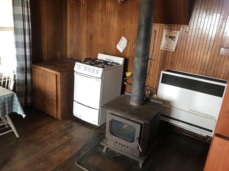 The cozy one room cabin offers a wood burning stove, propane range, dining table, and cabinet for cookware storage. 