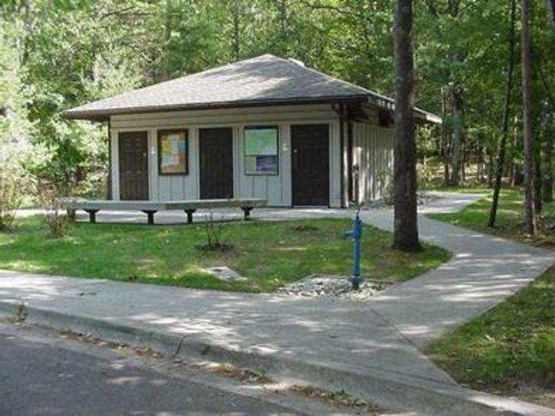 Front of comfort station showing sidewalk leading up to building, two benches, and water spigot