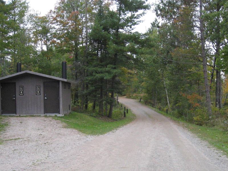 View of campground road and bathroom facility, near parking area for hiking trail, beach, and picnic area.