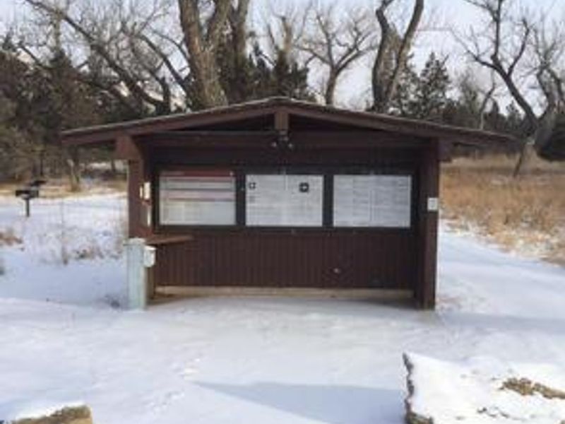 Picture of the Cottonwood Campground registration area. There is snow on the groups and the shelter is brown with three boards explaining the regulations. 