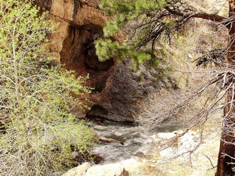 A cave in the rock face stands above a raging river.