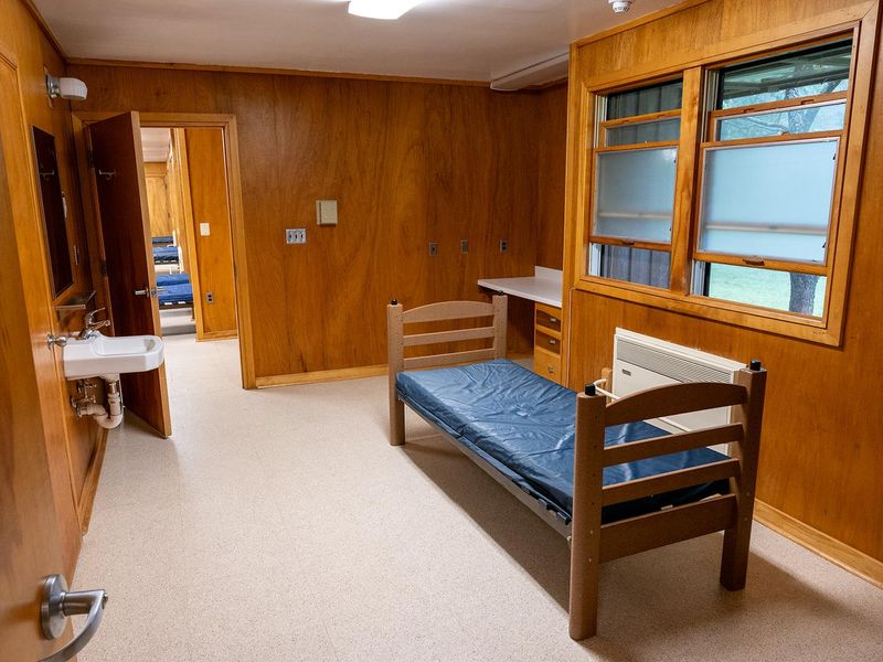 There are 2 individual rooms in each of the 4 dormitories.  These rooms contain a single bed with vinyl mattress, a closet, metal storage unit, small sink, wall mirror and wall mounted writing area (not visible)