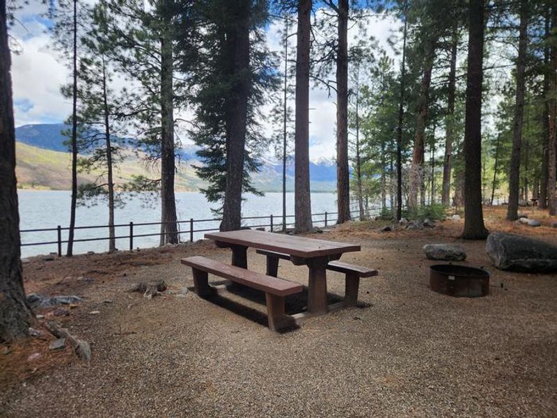 Campsite along lake with picnic table and fire ring