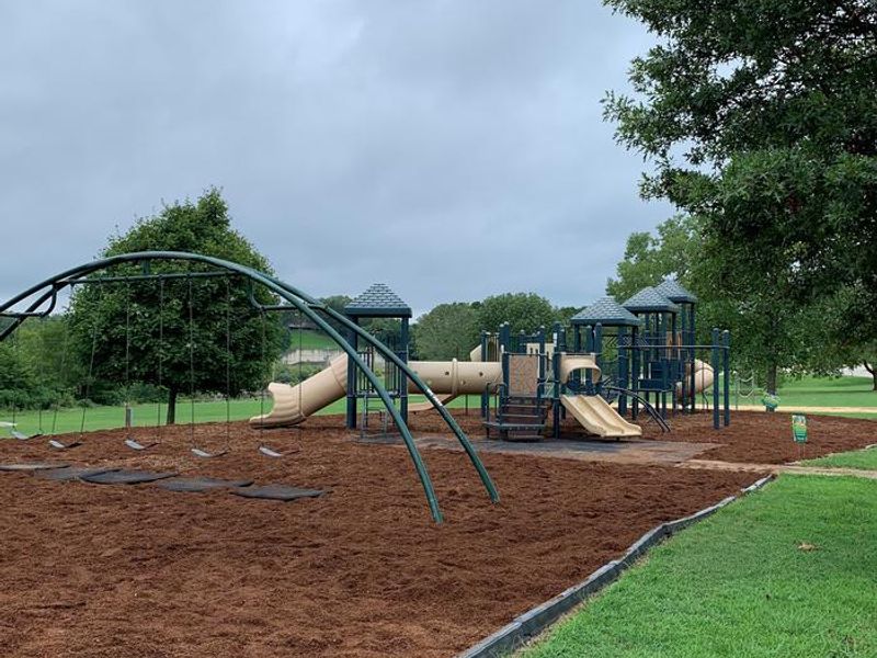 This playground area is near a volleyball court and  corn hole set.