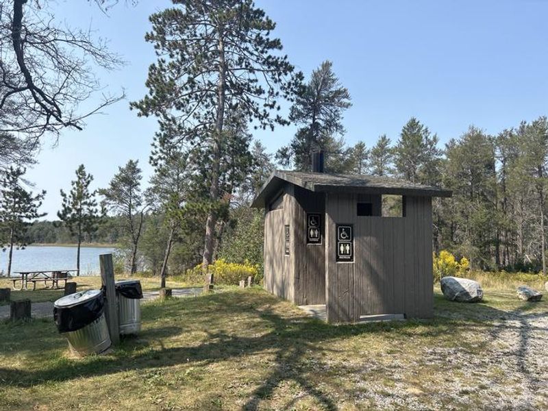 A photo of a vault toilet and trash receptacle at Wagner Lake (MI)