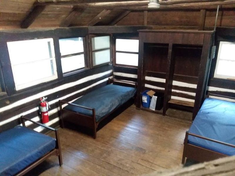 Interior of American chestnut log cabin.  Cabins have interior and exterior lighting, metal cots with vinyl covered mattresses, waste and recycle receptacles, and brooms.