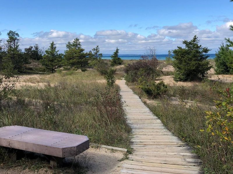 A wooden bench sits next to a boardwalk leading to Lake Michigan in the distance.
