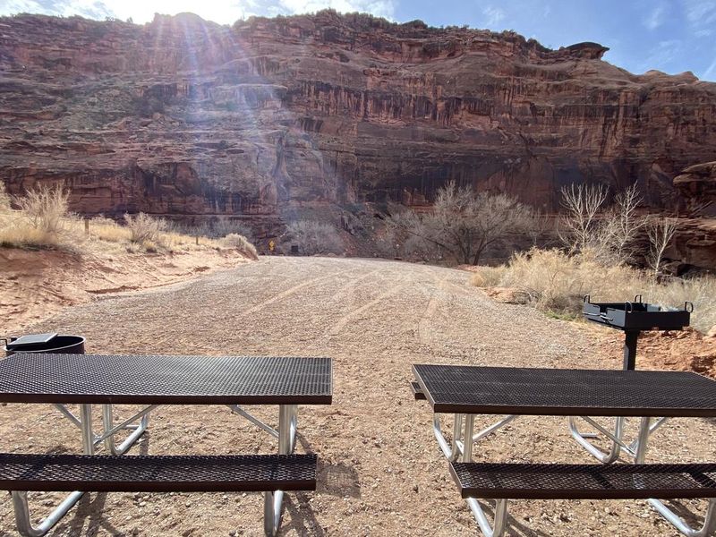 Group campsite, picnic tables, fire pit, and grill with sun setting behind cliffs in background