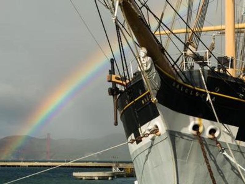 Balclutha's figurehead with rainbow and Golden Gate Bridge in background.