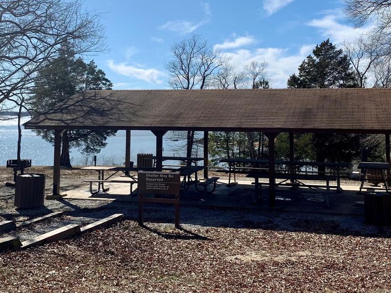 This is a picture of the OSAGE Picnic Shetler. This is a covered shelter with a water spigot located on the back of the shelter. There is also electricity at this shelter with outlets under the shelter. There are picnic tables under the covered shelter. You will find trash cans located throughout the park and near the shelter. There are steps that lead down to the shelter. 