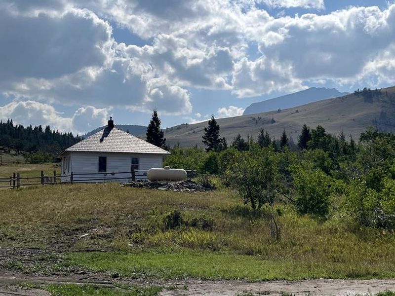 Small white cabin nestled in mountainous area with trees and clouds 