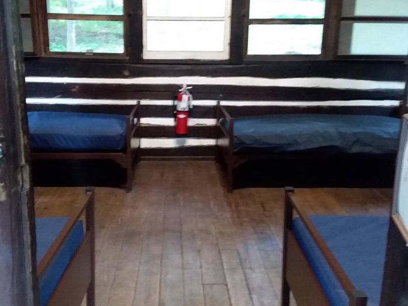 Interior of 4 person cabin from front door.  Wooden floor with 4 metal cots and vinyl covered mattresses.