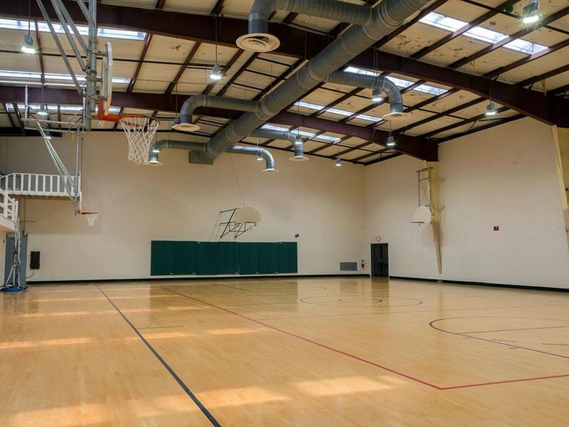 Interior view of gymnasium.  Standard size wooden marked floor with 6 basketball backboards/nets.  The building has air conditioning and heat.  Four small classrooms are accessible from the gymnasium.