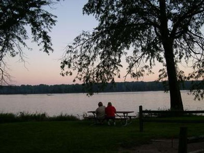 People at a picnic table at sunset overlooking the river.