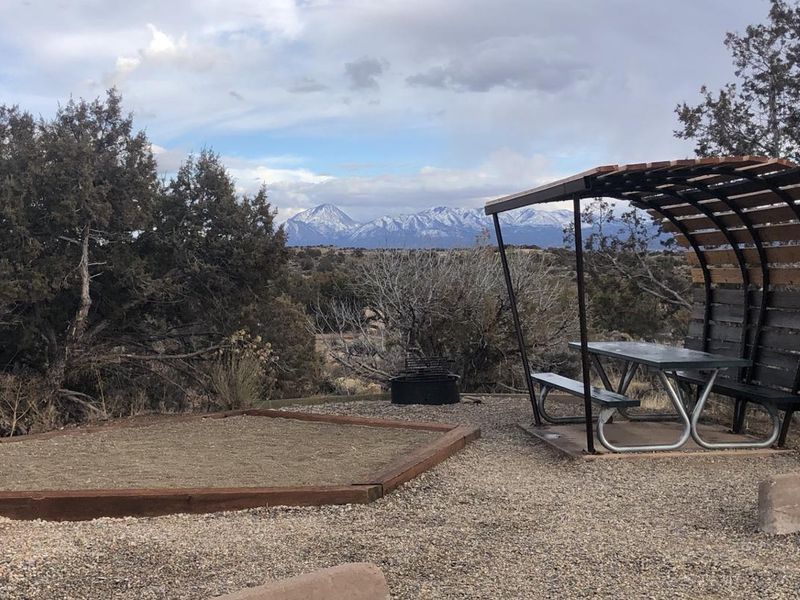 A tent pad and covered picnic table with a background of Sleeping Ute mountain range's snow-covered peaks.
