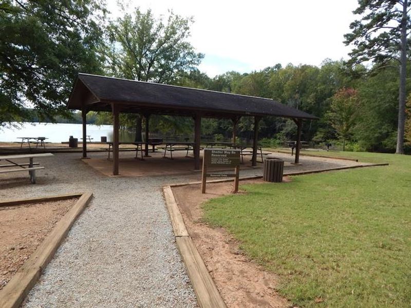 This is a photo of the Longwood Shelter. This shelter has picnic tables located under a covered shelter. There are trash cans located throughout the park and there are also grills on both ends of the shelter. 