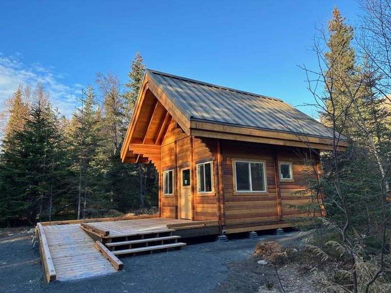 A side view of the two-story log cabin showing the ramp and stairs that lead up to the front porch.  