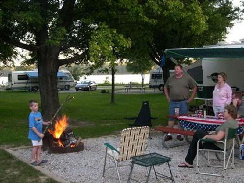 Young boy roasting marshmallows with adults watching at campsite.
