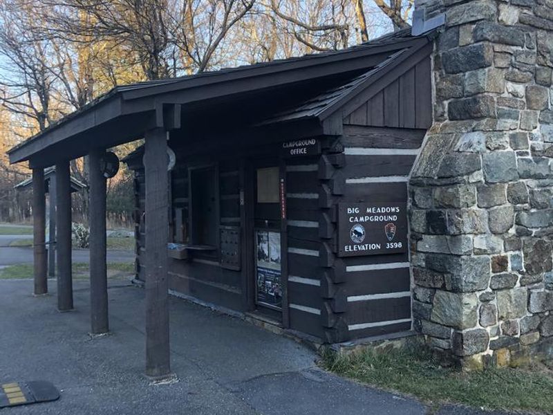 A wooden cabin with stone chimney and signs reading "Big Meadows Campground Elevation 3589" and "Campground Office".