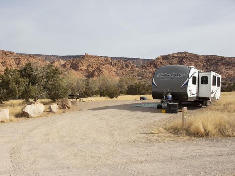 Campsite with trailer parking in parking area. Red rock cliffs line the horizon in the background.