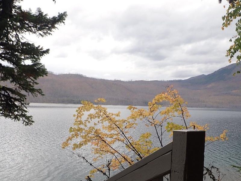 Lake McDonald with fall foliage in the foreground and mountains in the background.