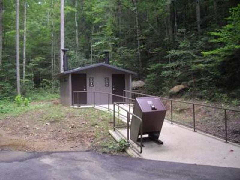 Brown bear-proof garbage can on paved walkway to newly installed vault toilet.