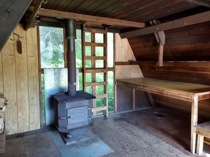 Interior of cabin with wood stove and showing table along side wall.